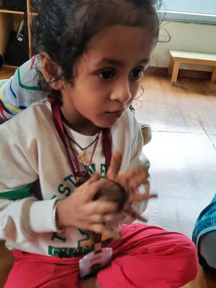 A child holds the clay Ganesha she is helping to create, her face full of concentration and wonder.