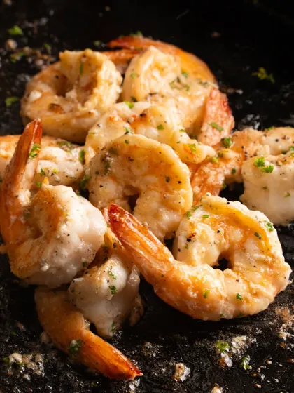 A close-up of butter garlic prawns, fresh from the kitchen. The dark, textured surface makes the prawns pop.
