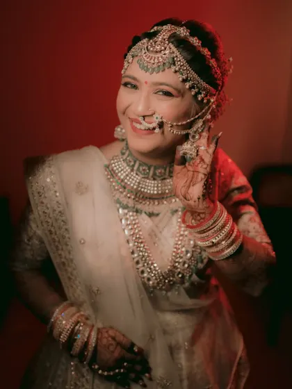 The bride gives a joyful 'salaam' pose, her smile radiant under a pop of red light.