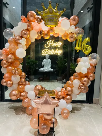 A sweet 16th birthday decoration with a rose gold and white balloon ring, topped with a crown foil balloon.