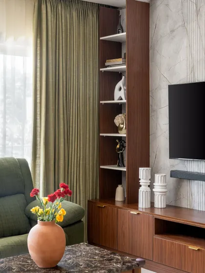 A close-up of the media unit in 'The Flux Abode', showing the combination of open and closed storage. The rich walnut finish adds warmth against the cool, textured wall.