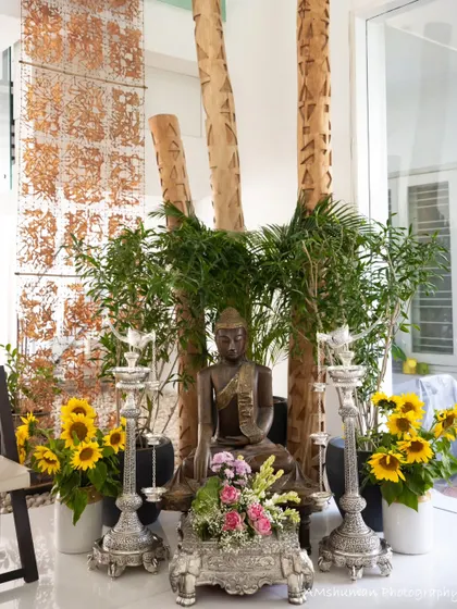 A serene and spiritual corner setup for a baby welcome, featuring a Buddha statue surrounded by sunflowers, traditional silver candle holders, and lush greenery.