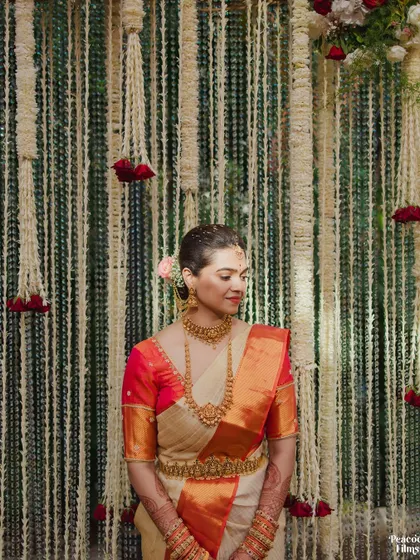 A serene portrait of the bride against a wall of hanging jasmine flowers, her traditional gold jewelry shining.