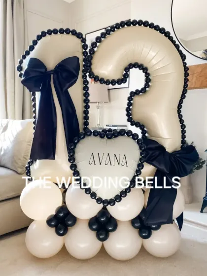 A chic and modern balloon bouquet for a 13th birthday. The black and white color scheme with large satin bows gives it a sophisticated look, and the personalized 'Avana' heart balloon makes it a unique centerpiece for the celebration.
