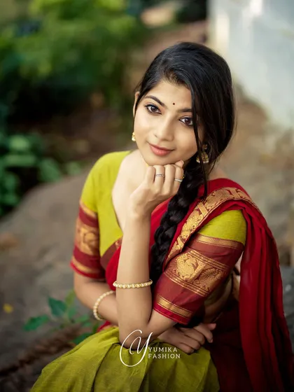 A candid moment of joy while modeling a traditional red and green half-saree. The natural, rustic setting complements the earthy tones of the Kanchi cotton fabric.