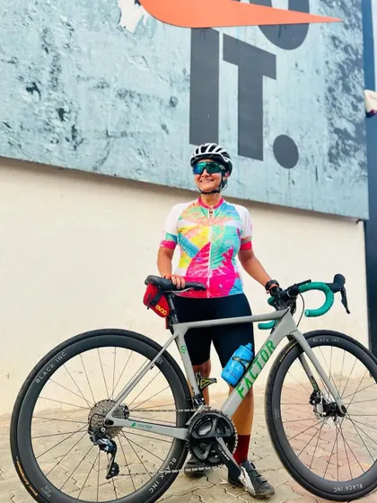 Our vibrant summer jersey in action. A member poses with her bike, showing off the colorful kit against a "Just Do It" backdrop.