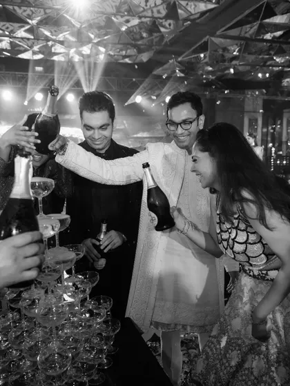 The joy of celebration is infectious. This black and white shot captures the couple and their friends at the champagne tower, a perfect moment from a Sangeet night designed for fun and connection.