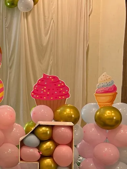 Fun candyland props including large cupcake and candy cutouts, surrounded by pink and gold balloons.