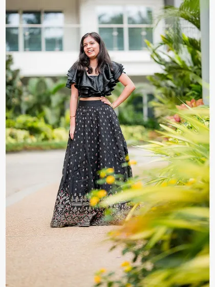 A stylish portrait of a young woman in a black lehenga, taken during a family photoshoot in a lush green setting.