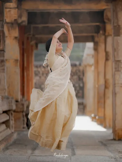 A bride-to-be, dressed in an elegant cream saree, leaps with joy in a stone temple hallway. This captures her personality and the happiness of the moment.