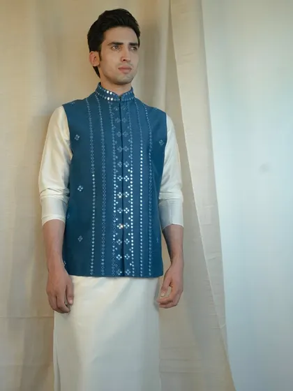 The fancy mirror work on this blue jacket pairs beautifully with a stylish silk kurta, creating a look of resplendent royalty.