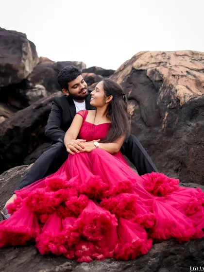 A romantic portrait of a couple seated on coastal rocks, lost in each other's gaze. The contrast between the formal attire and the rugged natural setting creates a striking visual for a pre-wedding album.