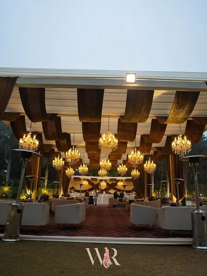 A wide view of the outdoor lounge area, with its striped brown and white ceiling, numerous chandeliers, and comfortable white sofas. The space was designed to be a grand yet cozy retreat for guests.