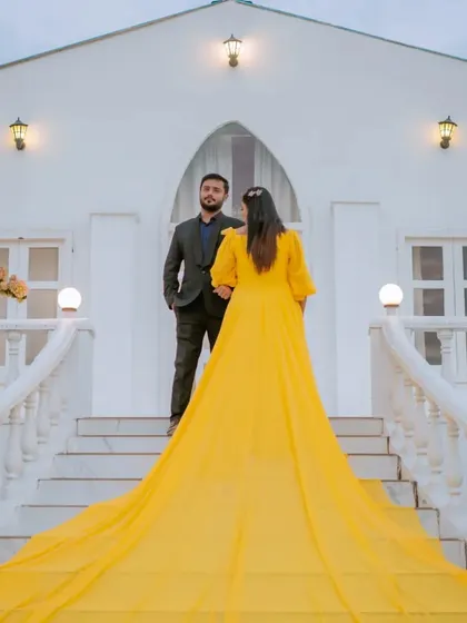 A dramatic shot from behind, showcasing the incredible length and color of the bride's yellow trail gown. This angle emphasizes the grandeur of the outfit and the unique location.