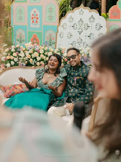 The happy couple seated in front of their stunning pastel Mehendi backdrop, sharing a laugh with their guests.