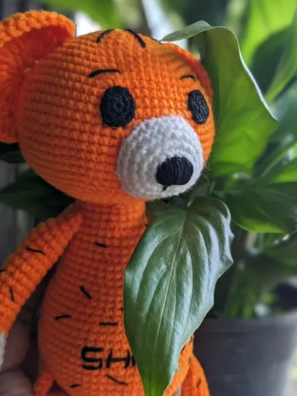 A playful shot of the custom tiger amigurumi peeking from behind a large green leaf.