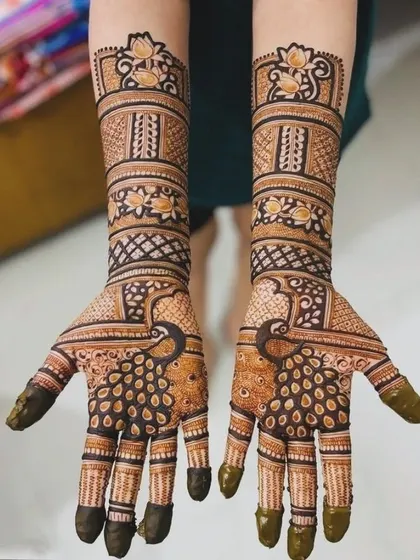 A beautiful peacock-themed bridal mehndi. The fanned-out tail of the peacock covers the fingers, creating a unique and elegant effect.