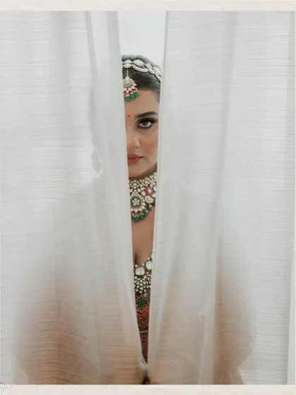 An artistic portrait of the bride peeking through a sheer white curtain.