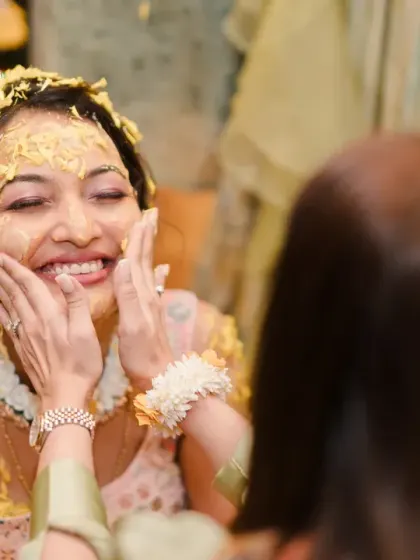 The bride's face is lovingly smeared with haldi by her friends and family. Her joyful expression shows she's enjoying every moment of the playful ritual.