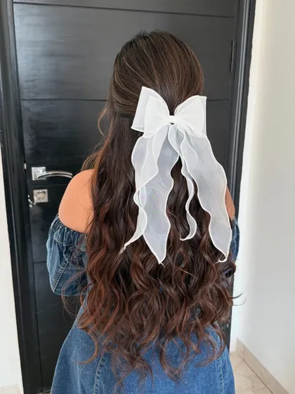 Sometimes, a simple accessory is all you need. A delicate white bow pinned into long, wavy hair, enhanced with extensions for fullness, creates a soft and feminine look.