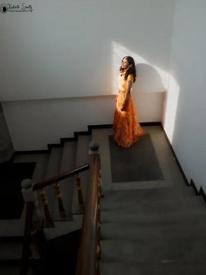 An artistic shot of a bride in her Haldi outfit, standing on a staircase. The strong shadows and light create a dramatic, high-contrast image that feels both modern and timeless.