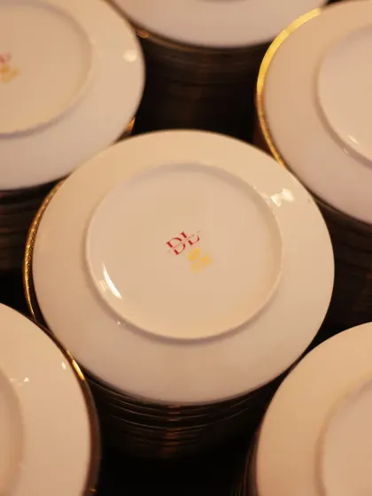 A stack of our custom-branded plates, ready for service. The simple "DL" logo signifies a standard of quality and elegance that we uphold in every aspect of our work.