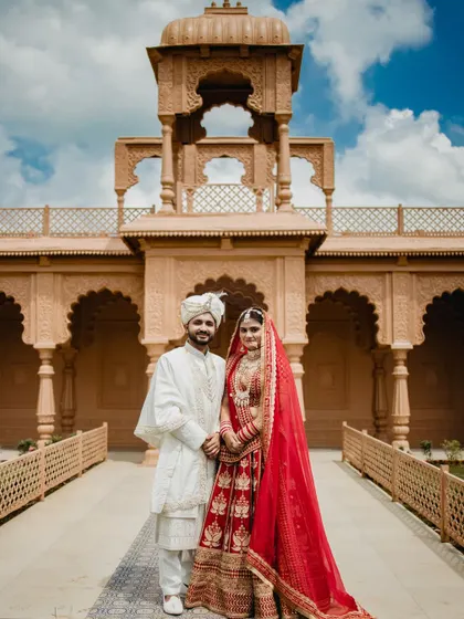 A classic, formal portrait of the bride and groom in front of the grand venue. Their pose is elegant and timeless, a perfect keepsake of their royal wedding day.
