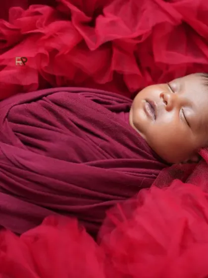 A different angle of the royal newborn session, capturing the baby nestled in a sea of red fabric. The tiny crown adds a touch of majesty to this adorable sleeping pose.