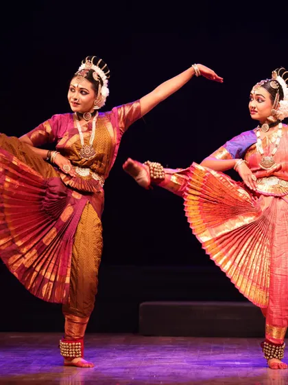 Two dancers in a dynamic pose with legs extended, their vibrant pleated costumes fanning out beautifully. A moment of pure artistry from the Sadhana festival.