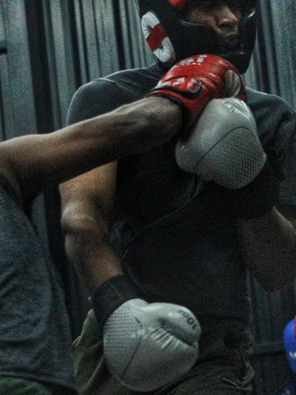 A body shot lands during sparring. The female boxer in the background watches and learns.
