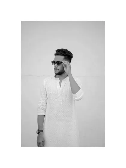 A minimalist black and white portrait. The stark background and the simple action of adjusting his sunglasses create a cool, confident, and modern look.