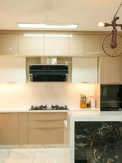 This kitchen from the "Golden Feather" villa features glossy, neutral-toned cabinets and a striking black marble accent on the breakfast bar. The quirky bicycle-themed pendant light adds a touch of whimsy and personality.