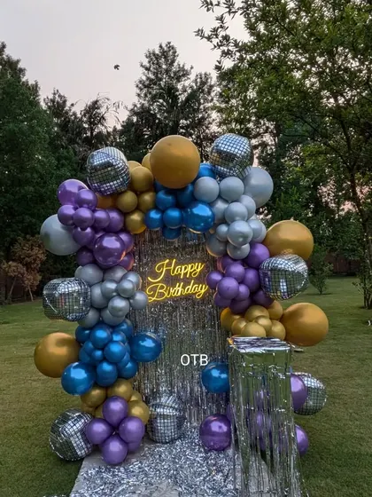 An outdoor party setup with a disco vibe. This backdrop uses a silver shimmer panel and a colorful balloon arch with disco ball accents for a fun, retro feel.