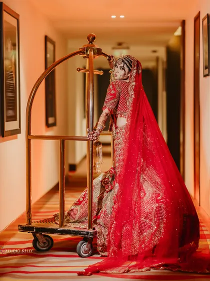 An artistic and dramatic shot of the bride in her red lehenga, posing with a luggage trolley in a hotel corridor.