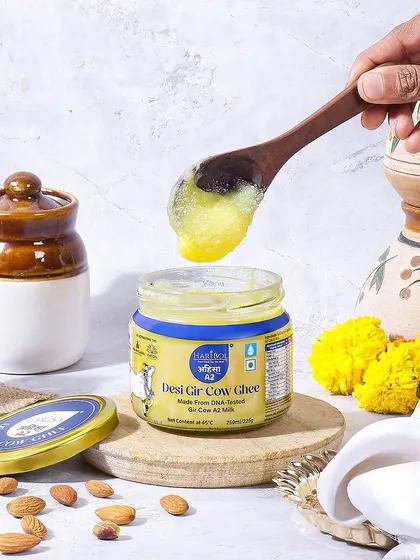 A festive and traditional setting for Desi Gir Cow Ghee. The use of marigold flowers, almonds, and traditional pickle jars creates a cultural context, positioning the ghee as a pure and auspicious product.