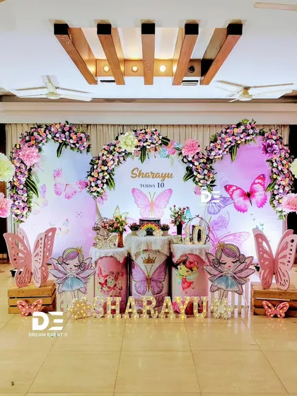 A grand butterfly and fairy-themed stage for a 10th birthday, with large floral arches, fairy cutouts, and giant paper flowers.