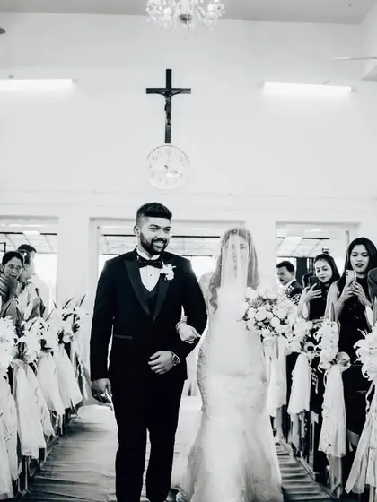 A black and white shot of the wedding processional down the church aisle. The composition leads the eye directly to the couple.