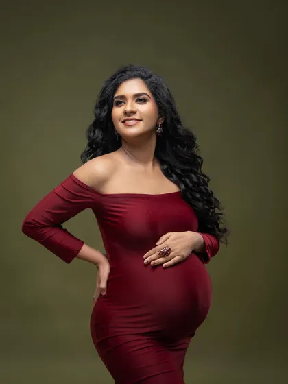 A classic portrait in a deep red off-the-shoulder gown. The rich color and simple olive backdrop create a warm and intimate feel.