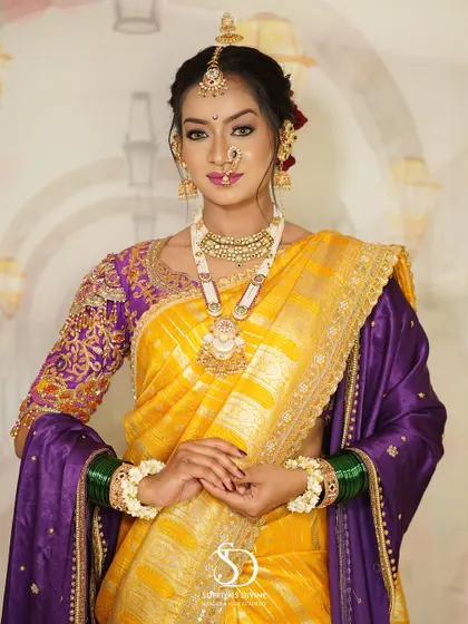A full-length view of a traditional Marathi bride. The look is complete with a vibrant yellow and purple saree, green glass bangles, and floral bracelets, all tied together with flawless makeup.