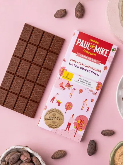 A milk chocolate bar sweetened with dates, styled on a soft pink background with cocoa beans to highlight its natural ingredients.