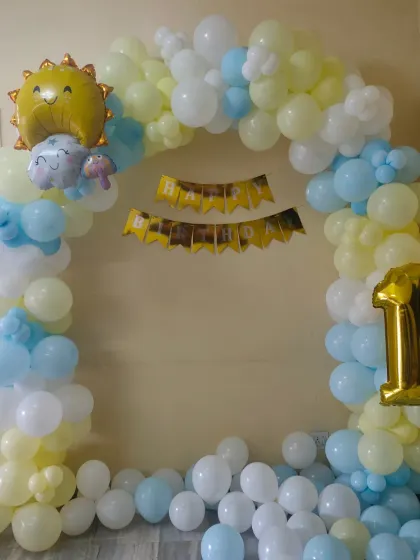 A cute sun-themed basic balloon arch in yellow and blue for a first birthday party at home.