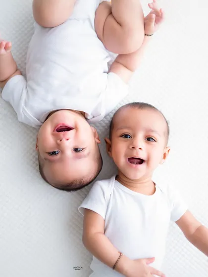 Two happy twin babies lying side-by-side, one upside down, making for a playful and unique portrait.
