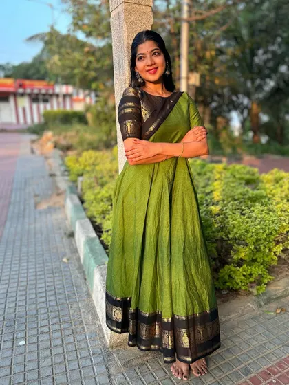A full-length shot of a green cotton kurti with a black and gold traditional border. The outfit is styled as a dress, showing its versatility and elegance.