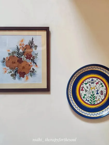 An example of how my art can be styled. Here, a Warli art wall plate is paired with one of my framed pressed flower pieces.