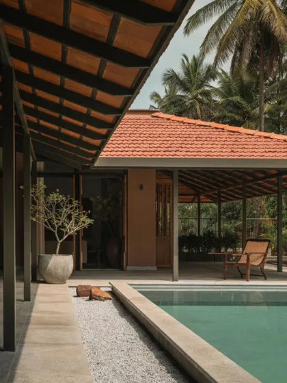 The covered veranda along the pool offers a shaded spot to relax. The design uses simple steel posts and a traditional tiled roof, blending modern and vernacular architectural styles.