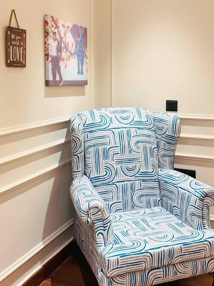 A cozy reading corner in a bedroom, featuring a comfortable wingback chair with a modern blue and white pattern, perfect for unwinding with a book.