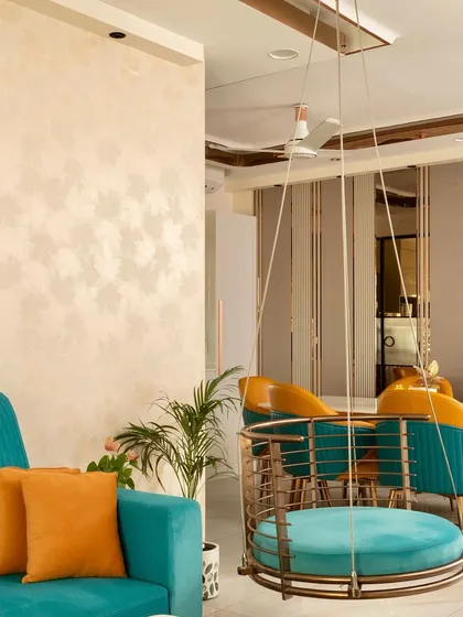 A vibrant living room with a teal sofa, a matching circular swing, and pops of orange, creating a sophisticated and comfortable space.