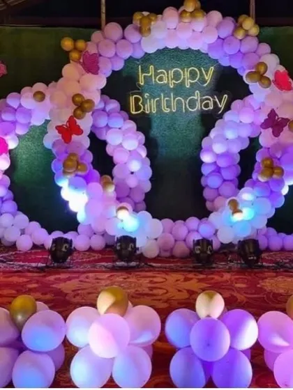 An intricate triple-ring balloon backdrop in shades of purple. This unique design with butterfly accents and a neon sign creates a stunning photo opportunity.