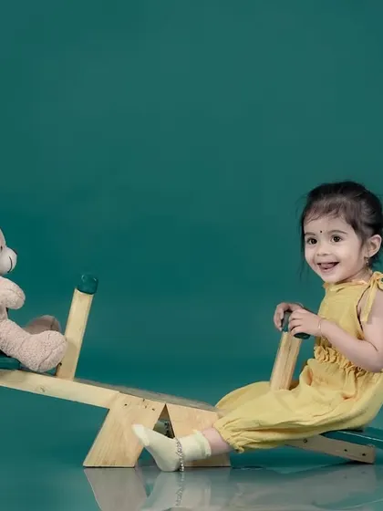 A sweet girl playing on a seesaw with her teddy bear against a simple, solid-colored backdrop in our studio.