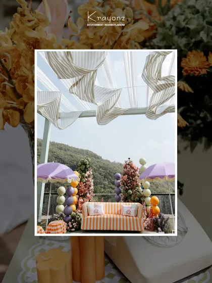 The decor for a colourful Mehendi, featuring a striped sofa, pastel balloon arrangements, and purple umbrellas, all set against a beautiful mountain view.